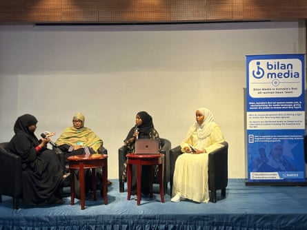 Four women sit in chairs next a sign for Bilan media