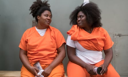 Danielle Brooks with Adrienne C Moore in Orange is the New Black; sitting side by side and both wearing orange prison tunics and trousers, and white T-shirts.