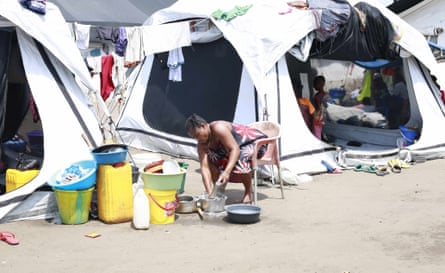 A woman washes a metal dish next to a row of tents