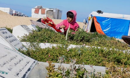 A small girl next to graves in the sand with tents in background