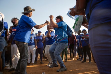 People in blue T-shirts dance at a rally