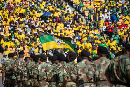 Soldiers stand in the foreground as huge crowds wearing yellow, black and green attend a rally