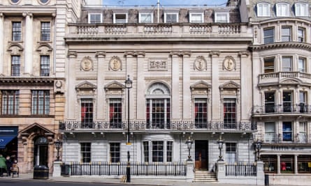 White’s on St James’s Street, London: an ornate stone building sitting behind railings with steps up to its entrance, lanterns at the gateway, wrought-iron balconies, tall first-floor windows with columns to either side, and architectural carvings above the windows