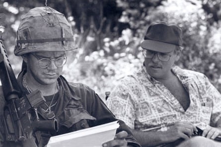 Tim Robbins in fatigues holding a rifle reading a script, next to Rubin who is in open neck shirt and baseball cap.