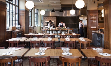 Tables set with plates and cutlery with chefs preparing food in the background