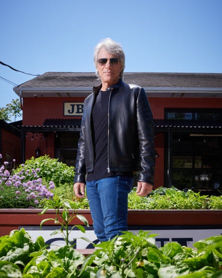 Portrait shot of Bon Jovi standing up surrounded by raised beds of green herbs and other plants.