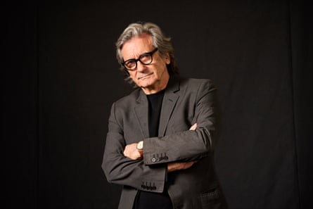 Griffin Dunne from waist up with arms folded looking askance at the camer