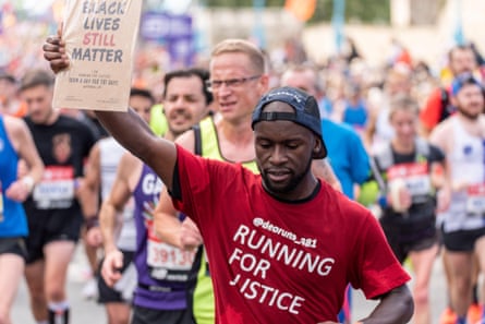 A man running in the London marathon holds up a placard reading Black Lives Still Matter