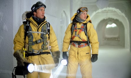 Two men dressed in cold weather survival clothes holding torches in a frozen building