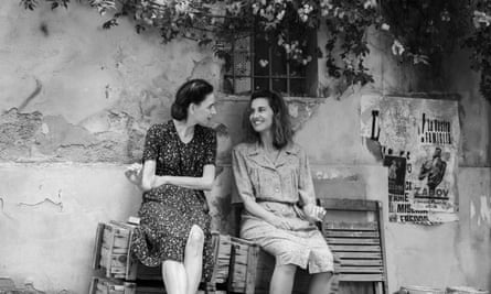 Monochrome image of two young women sitting on a bench by a wall talking to each other