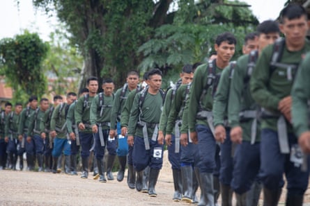 A line of Indigenous men marches down a street wearing green uniforms