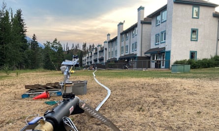 A water hose in front of white housing as night falls, with forest on the left