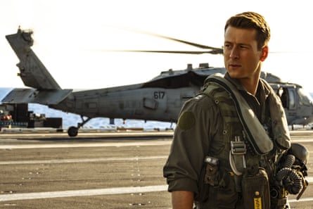 Powell, in military uniform and short hair brushed to one side, stands in front of an army helicopter looking to his left with a serious expression