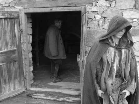 The Turin Horse (2011). A woman wearing a cape with her hood covering half her face walks away from an open door showing a man looking back over his shoulder