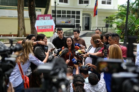 reporters holding microphones and video cameras surround woman wearing red