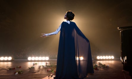 Angelina Jolie is surrounded by flowers on stage with her back to the camera