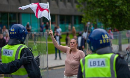 A woman flies an England flag in front of a line of riot police.