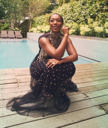 Naomi Ackie crouches by a poor wearing a black and gold gown