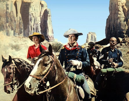 A woman, a white man and a black man ride horses in Monument Valley