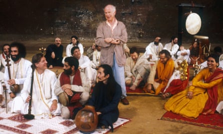 Peter Brook is surrounded by people in classical Indian dress sitting on rugs on stage