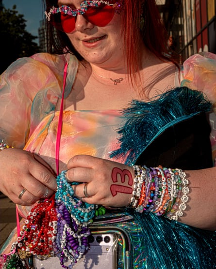 A woman in heart-shaped, glittery sunglasses and a multicoloured dress holds a bundle of friendship bracelets and a glitter-fringed garment