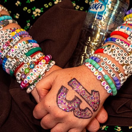 Closeup of a fan’s clasped hands, with ‘13’ written on the top hand and the arms covered with friendship bracelets