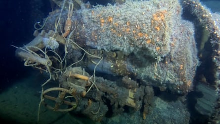 Pipes and a locking wheel are visible under barnacles on one side of the wreck