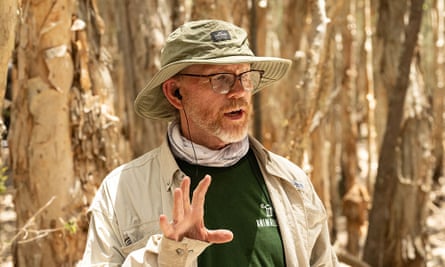 man in a hat gestures in front of trees