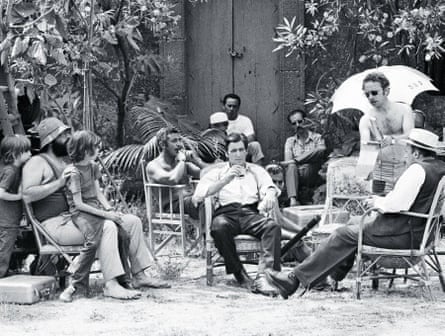 A black-and-white image of actors, the director and others, including two children sitting in a garden on a film set