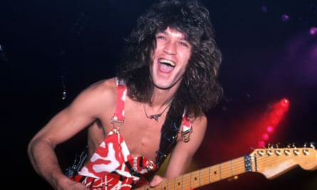 A man wearing red and white overalls smiles as he plays guitar on stage