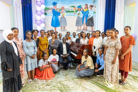 A group of girls and women pose around a piano with Girma Yifrashewa