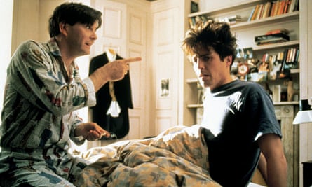 Hugh Grant, in a T-shirt and tousled hair, sits up in bed while James Fleet points a finger at him in a scene from Four Weddings and a Funeral