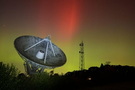 A large radio telescope under green and orange hues