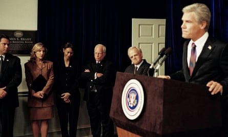 film still of a man in a suit standing at a podium as people look on