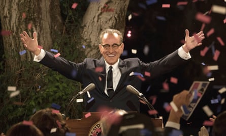 a man in a suit with his arms raised before a crowd as confetti flies in the air