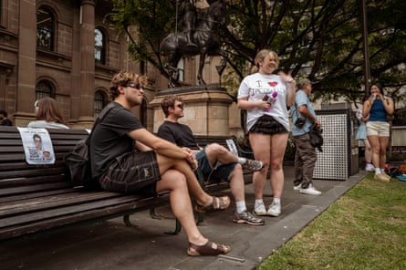 Alicia speaks to two men on a park bench.