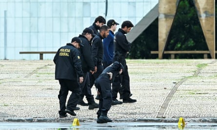 Seven men in black uniforms walk across a stone forecourt looking closely at the ground