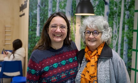 smiling woman, 39, in a woollen jumper with knitted pattern of alien faces and space invaders, with her grey-haired mother, 78, who wears an orange scarf with pattern of black bats