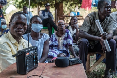 A group of people sit listening to a radio.