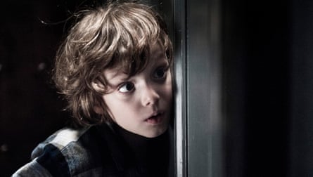 A close up of Noah Wiseman, with tousled brown hair, peeking from behind a door frame with wide eyes.