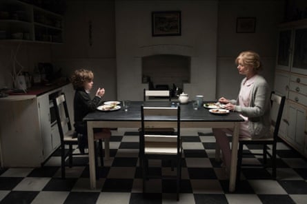 A small boy and an adult woman sit across from each other at a dining table in a kitchen, with a checkered black and white floor.