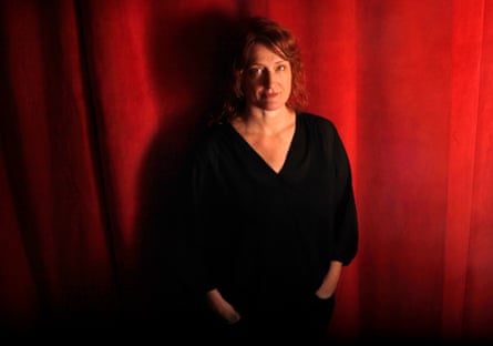 Jennifer Kent stands in front of a red curtain, dressed in black, looking slightly upwards to the camera.