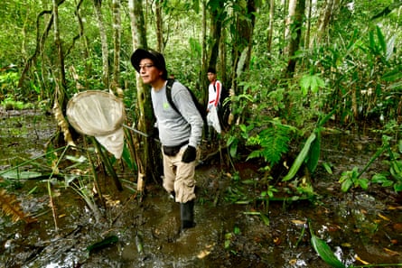 Two people stand ankle deep in mud in a forest with large nets in hand