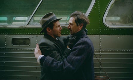 Two men in 40s-style clothing embrace alongside a bus