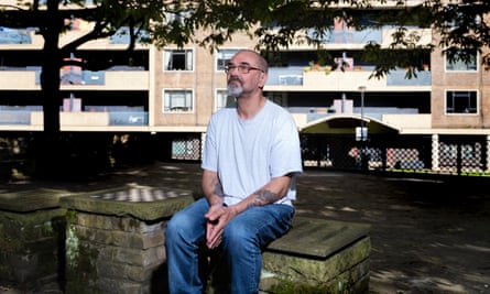 Andrew Malkinson: he sits on a brick wall in a green space with trees and a block of flats behind him