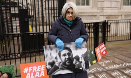 Soueif holds a picture of her son Alaa Abd El Fattah beside a #Free Alaa placard with black railings behind