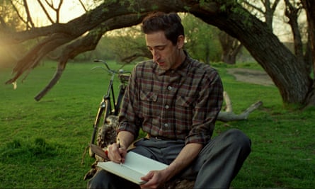 Adrien Brody writes in a book outdoors in The Brutalist