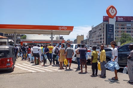 A long line of people wait at a petrol station in the sun