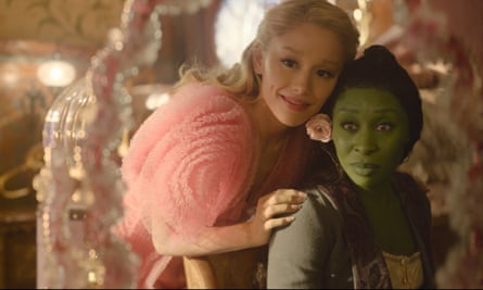 a woman with green skin and a blonde woman in pink look in a mirror