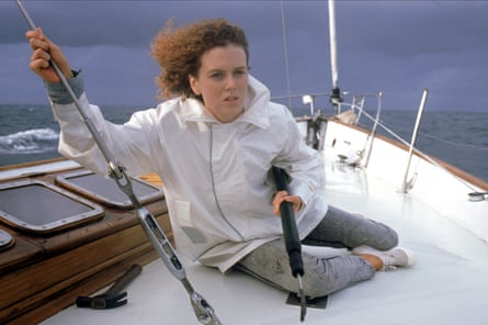 A woman sits on the deck of a small yacht, with the wind in her hair.